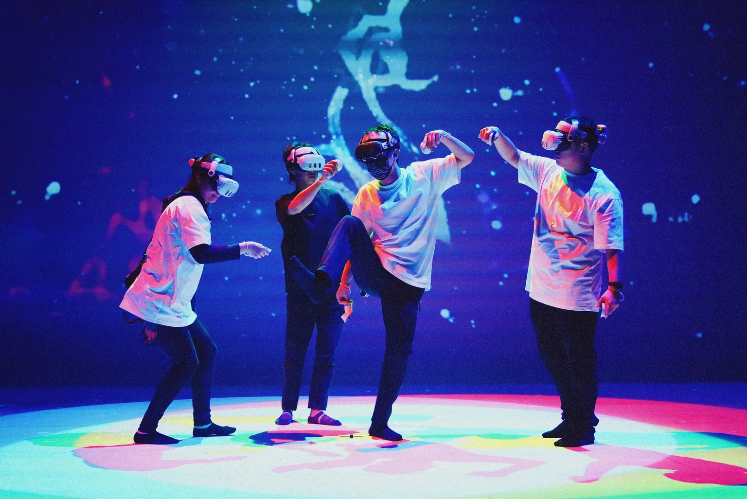 Four participants wearing VR headsets move and stretch under colourful stage lighting in 8 Degrees of Freedom