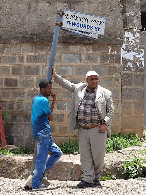 阿迪斯阿貝巴的實拍街牌或門牌。白底牌以上行衣索比亞文字、下行TEWODROS St.標示道路；St.是Street縮寫。