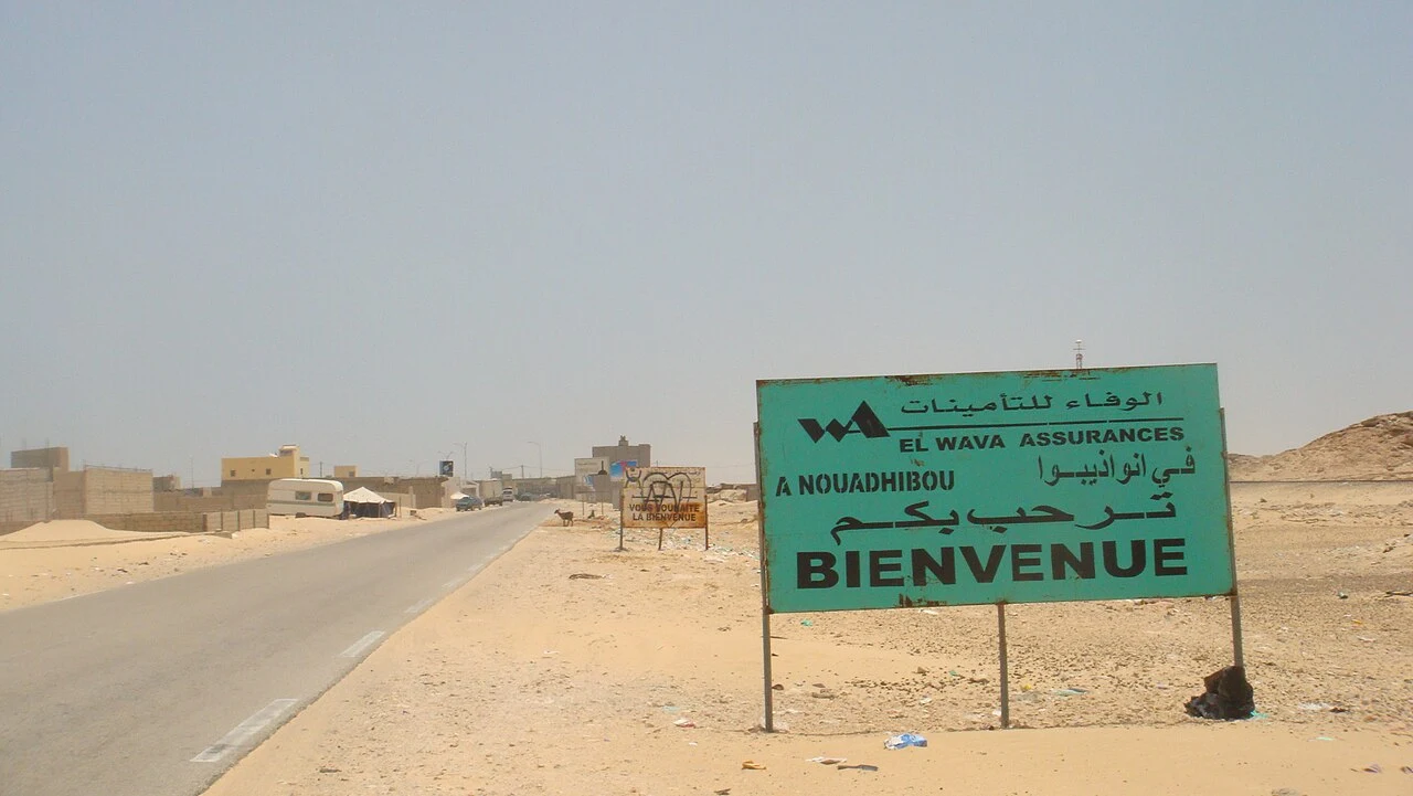 努瓦迪布實拍標示。À NOUADHIBOU表示在／到努瓦迪布，BIENVENUE為歡迎語；EL WAVA ASSURANCES是贊助品牌，並非道路名稱。