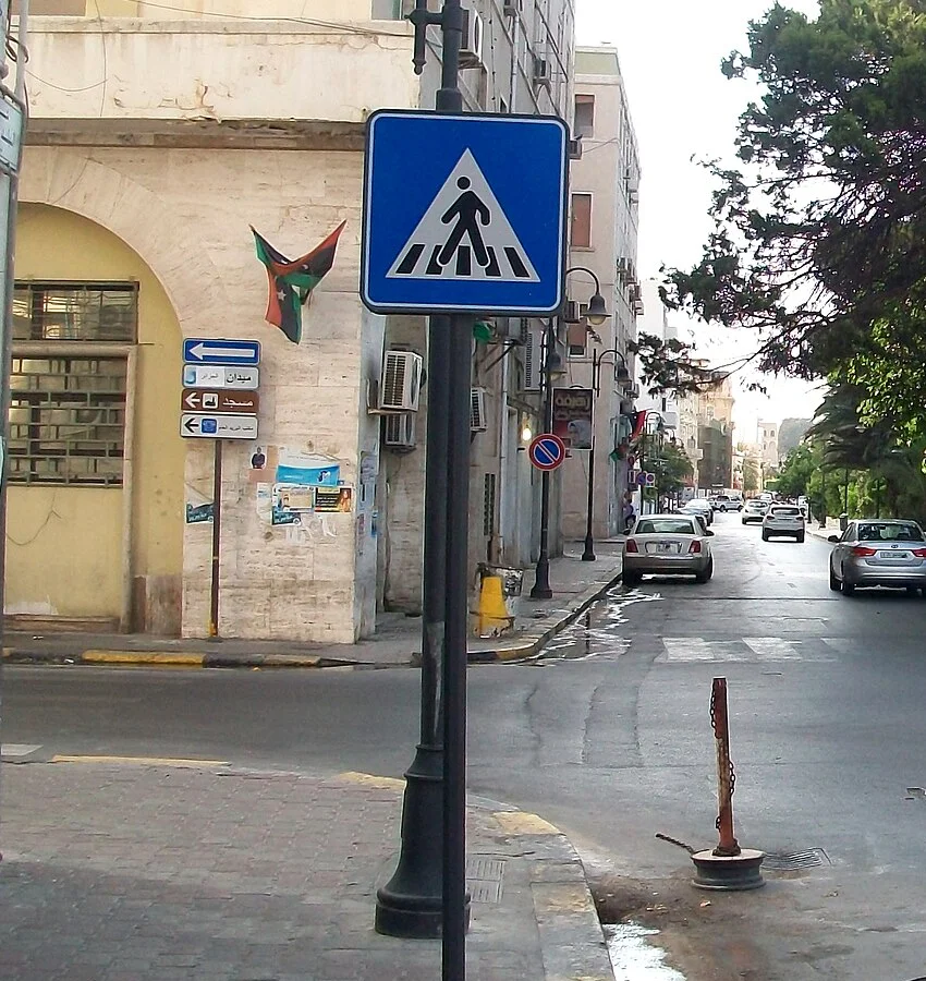 的黎波里街角實拍，分層指路牌的白色層寫著ميدان الجزائر阿爾及利亞廣場，上方另有藍色單行箭頭。