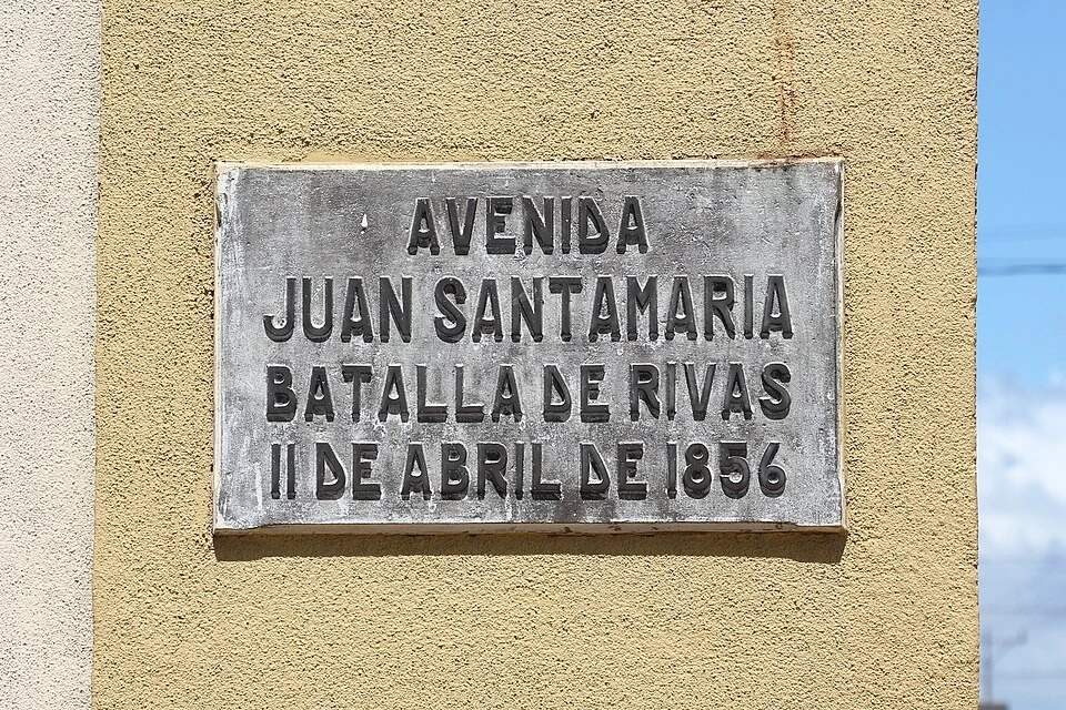 聖拉蒙街名標記。牌面依序可讀AVENIDA JUAN SANTAMARIA、BATALLA DE RIVAS、11 DE ABRIL DE 1856；AVENIDA表示大道。