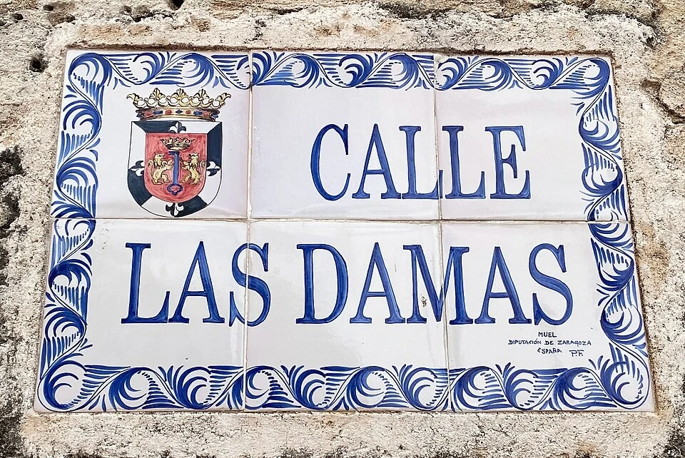 聖多明哥街名標記。大寫CALLE與LAS DAMAS分成兩行，CALLE是西班牙語的街；左上是彩色徽章。