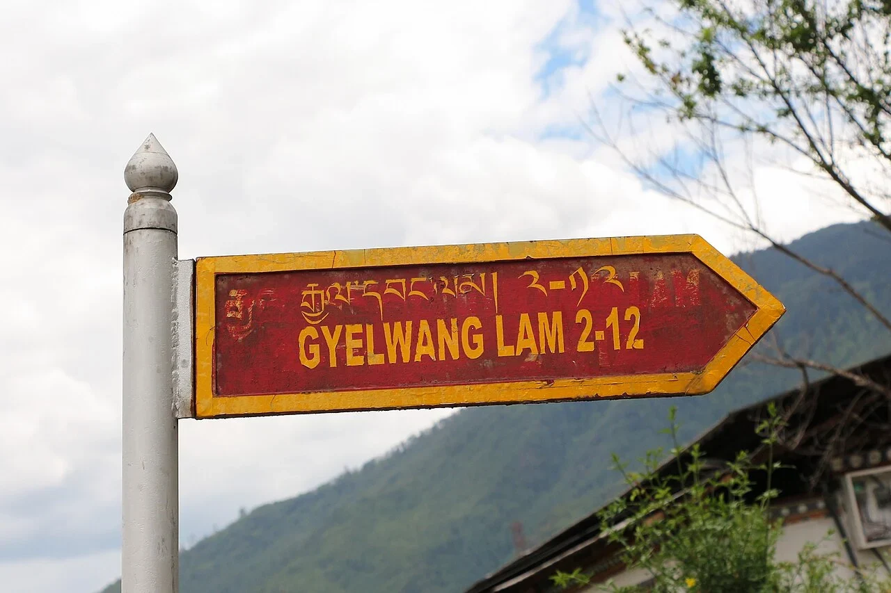 廷布：紅底黃框箭牌寫「GYELWANG LAM 2-12」，上行為宗喀文。