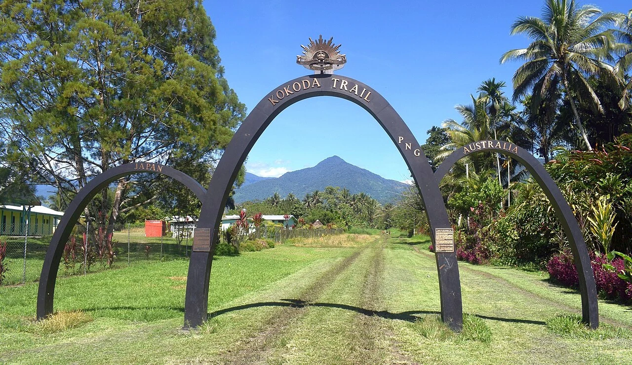 巴布亞紐幾內亞科科達端草地步道上，深色拱門以淺金字寫KOKODA TRAIL，兩側另有JAPAN與AUSTRALIA小拱。