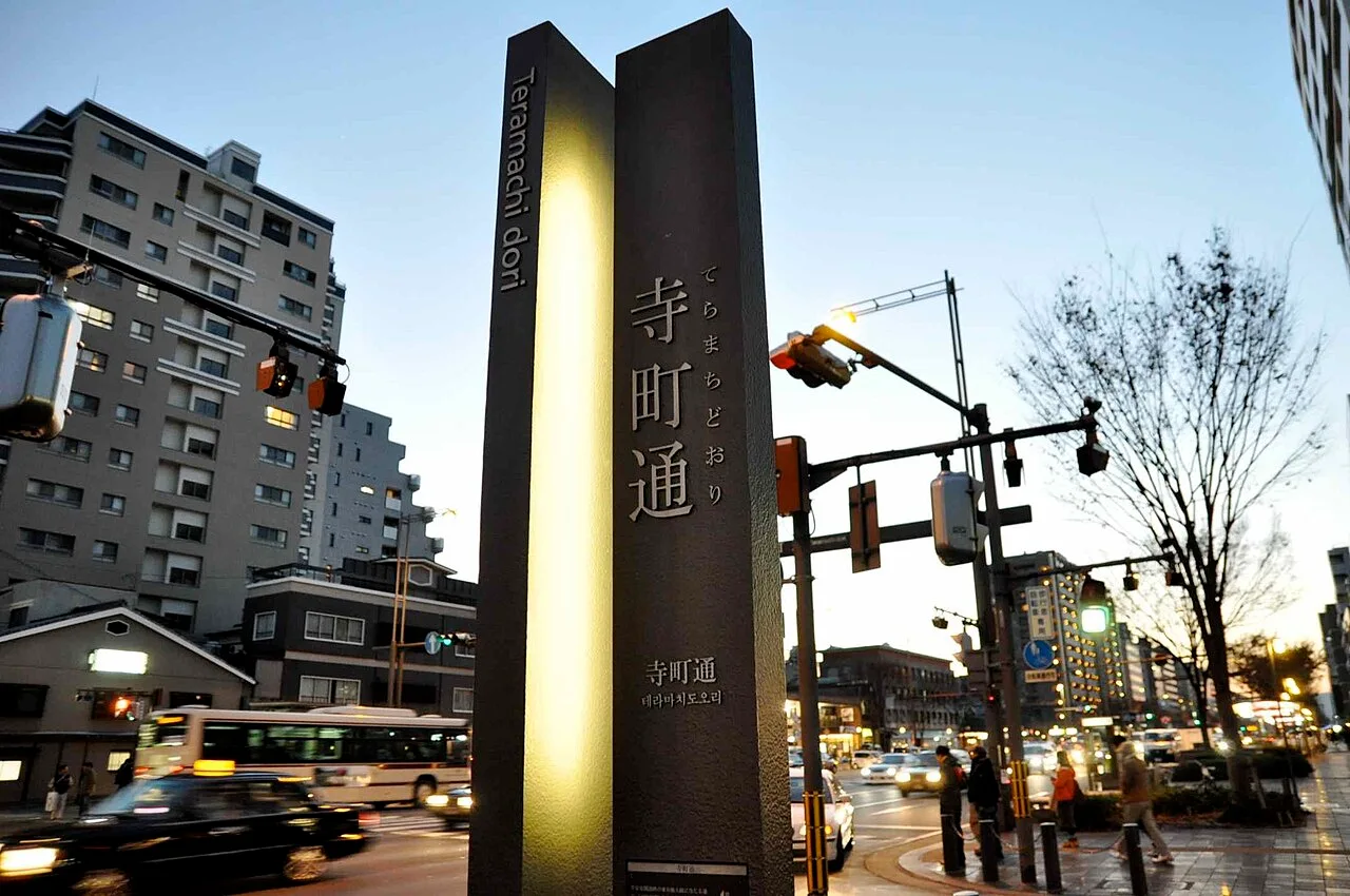 京都寺町通夜色中的黑色直立標示,寺町通直排文字與多語標示映在照明面板旁。