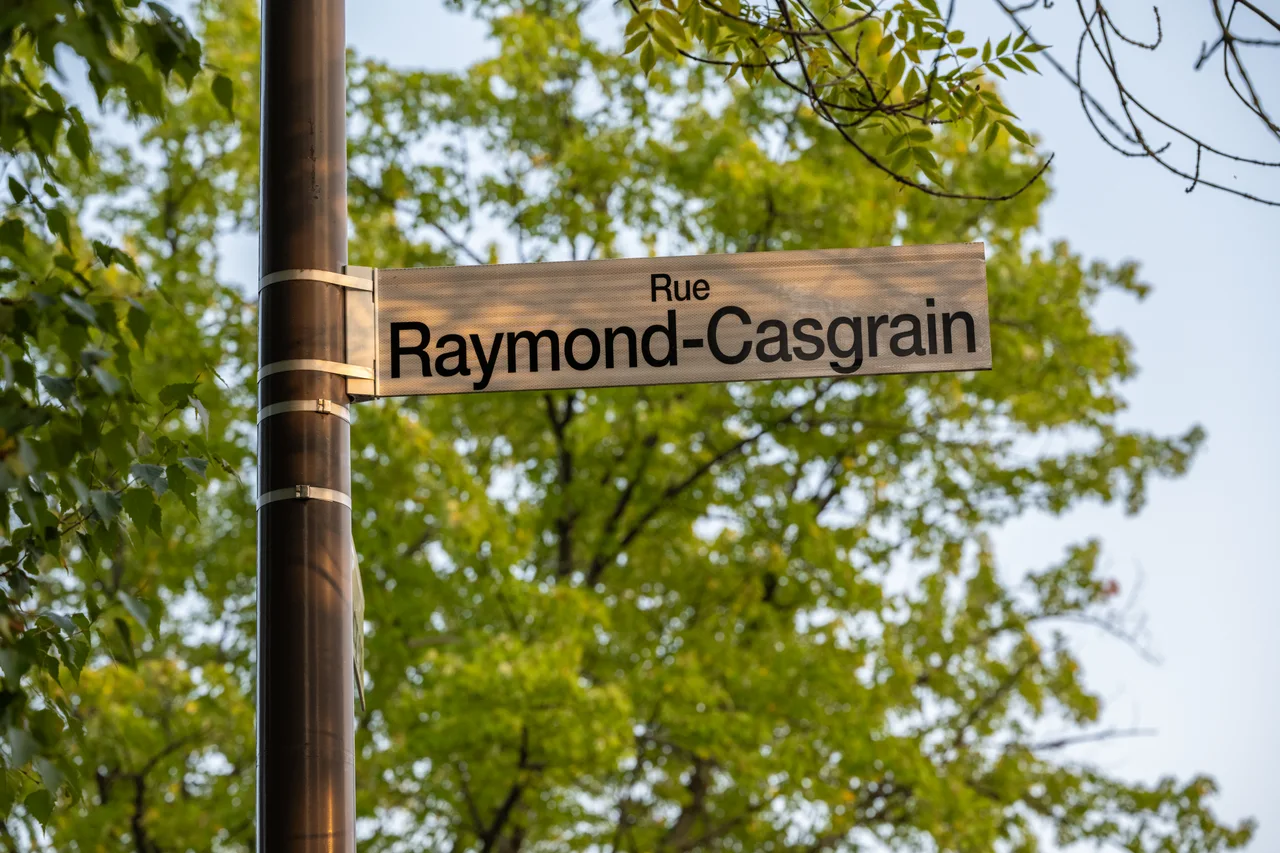 魁北克市淺底黑字Rue Raymond-Casgrain雙行街牌,背後是綠色樹葉。