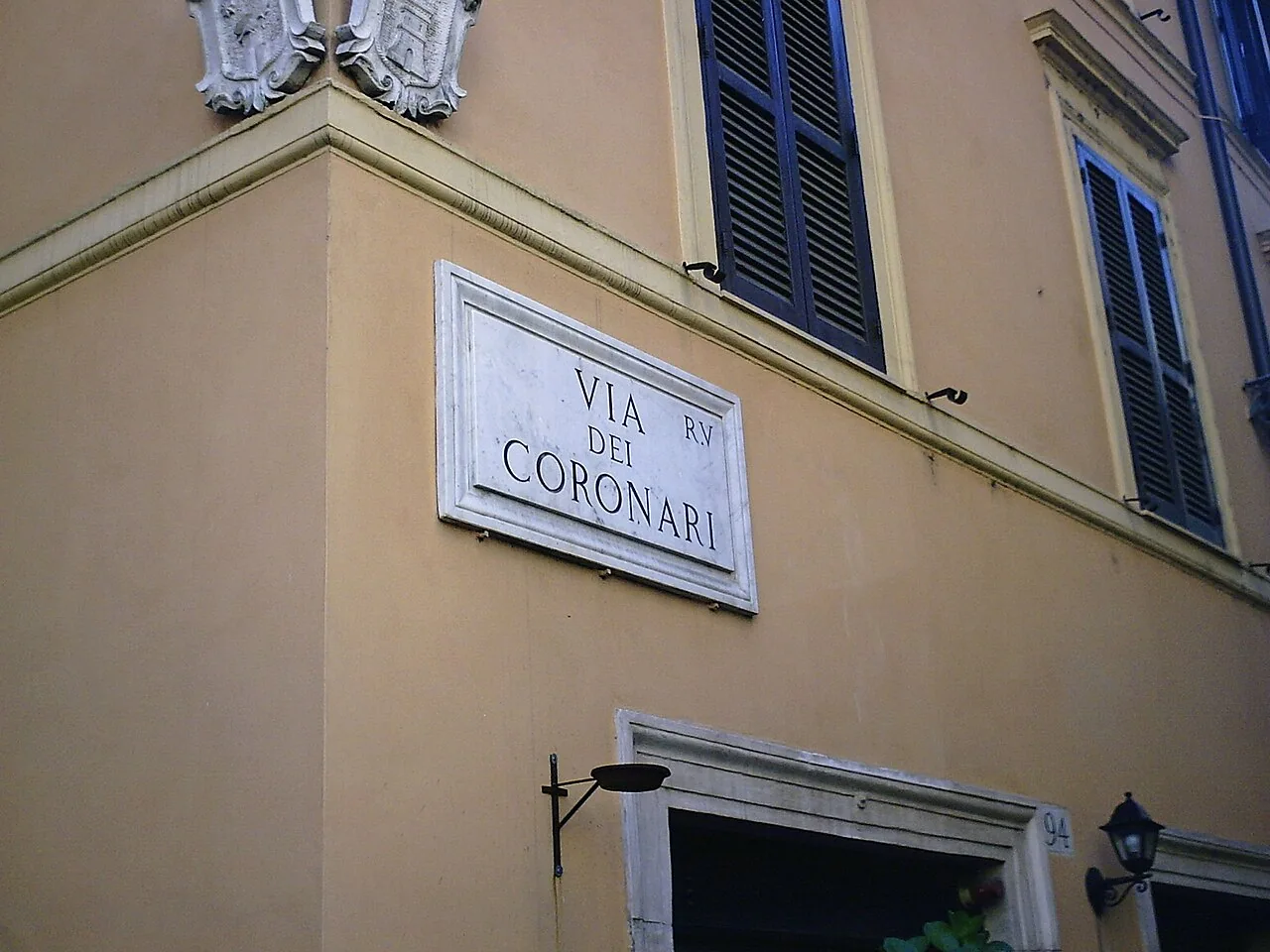 羅馬赭色牆面上的Via dei Coronari淡色石牌，街名分三行，右上有R.V小字。