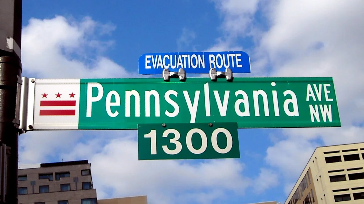 華盛頓綠底白字Pennsylvania Ave NW街牌，含1300街區數字與特區旗幟，上方是藍色疏散路線牌。