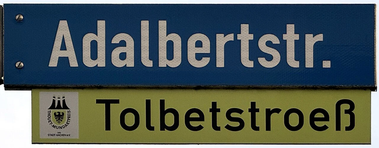 亞琛的實拍街牌。主牌「Adalbertstr.」是Adalbertstraße的縮寫;下方黃色副牌另列地方語拼寫,並非門牌。