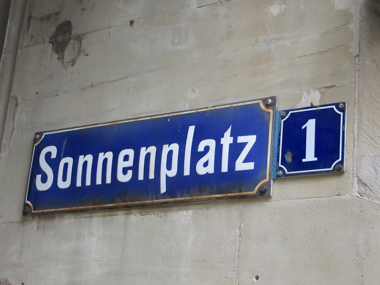 巴登巴登的實拍街牌。「Sonnenplatz」為廣場名，右側獨立小牌「1」是門牌；兩者相接但功能不同。