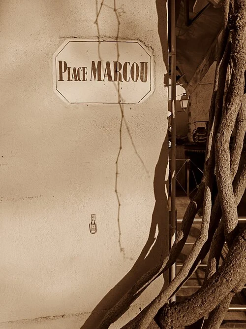 卡爾卡松的實拍街牌。牆面可讀「Place MARCOU」；Place表示廣場，並非人名的一部分。