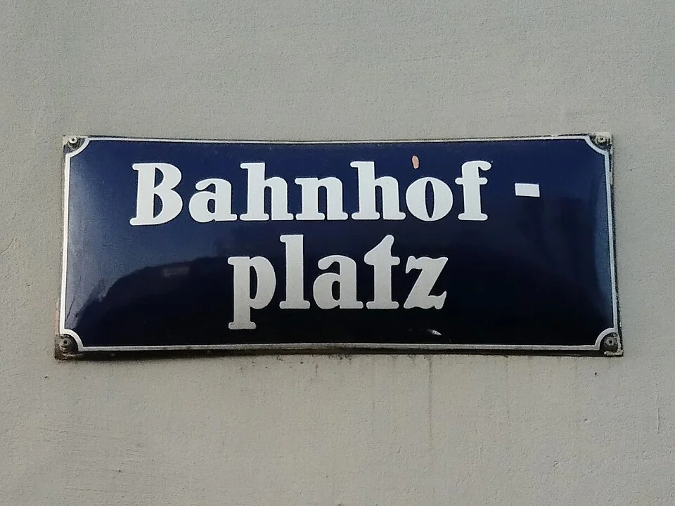 克雷姆斯的實拍街牌。「Bahnhof-platz」分兩行合讀為Bahnhofplatz，即車站廣場；中間連字號是換行處理。