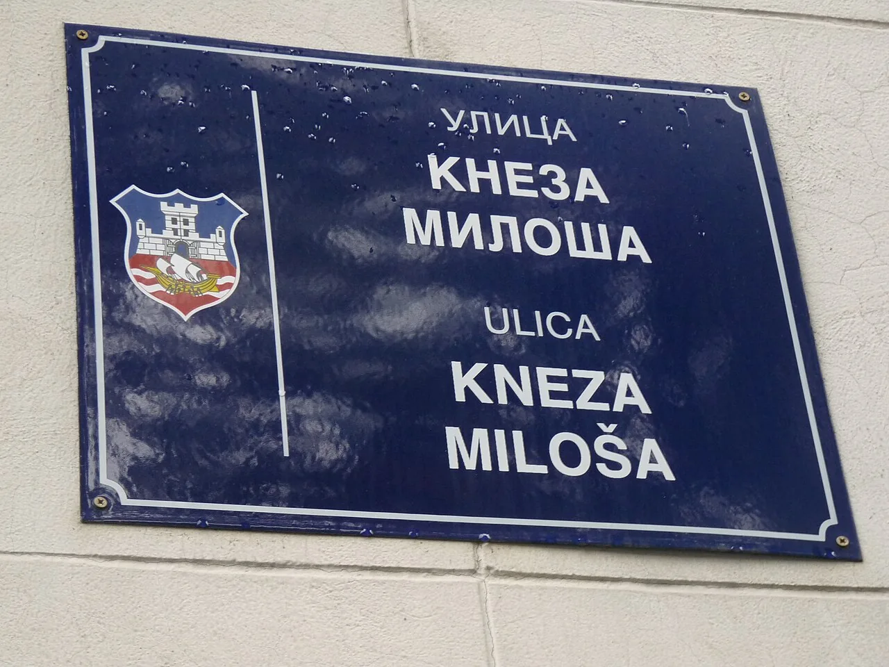 貝爾格勒藍底街牌，左有城市盾徽，右側以上下兩組字母寫出Kneza Miloša街名。