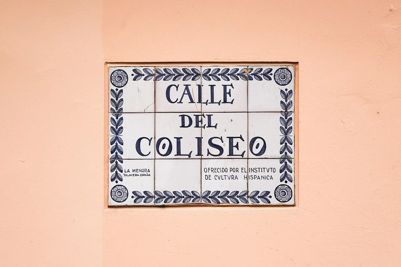 波哥大粉橘色牆上藍白拼接磚牌，三行寫CALLE DEL COLISEO，外圍有花葉紋，底部有捐贈說明。