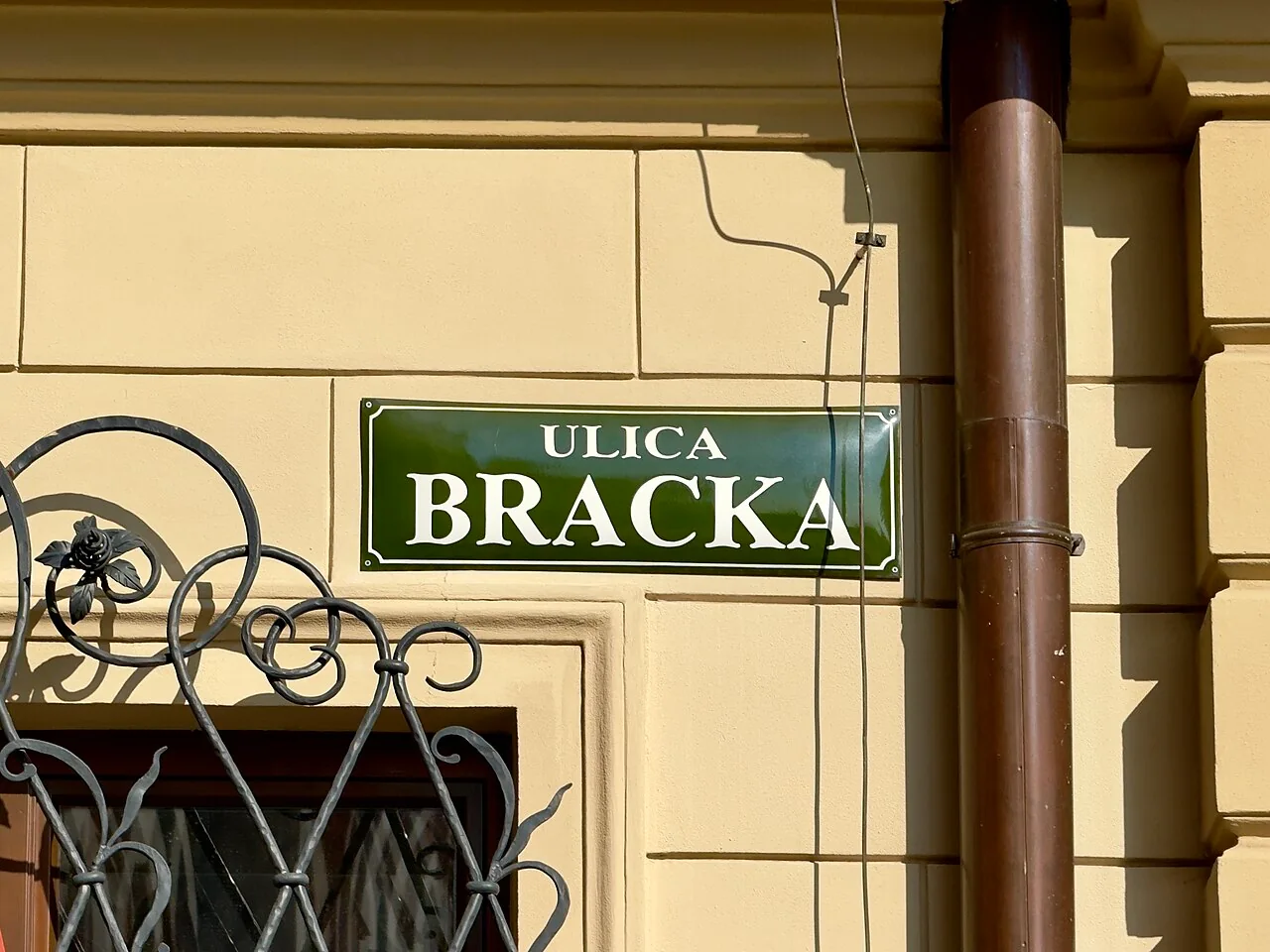 克拉科夫黃牆上的深綠街牌，上寫ULICA，下方大字BRACKA，四角有內縮白框。