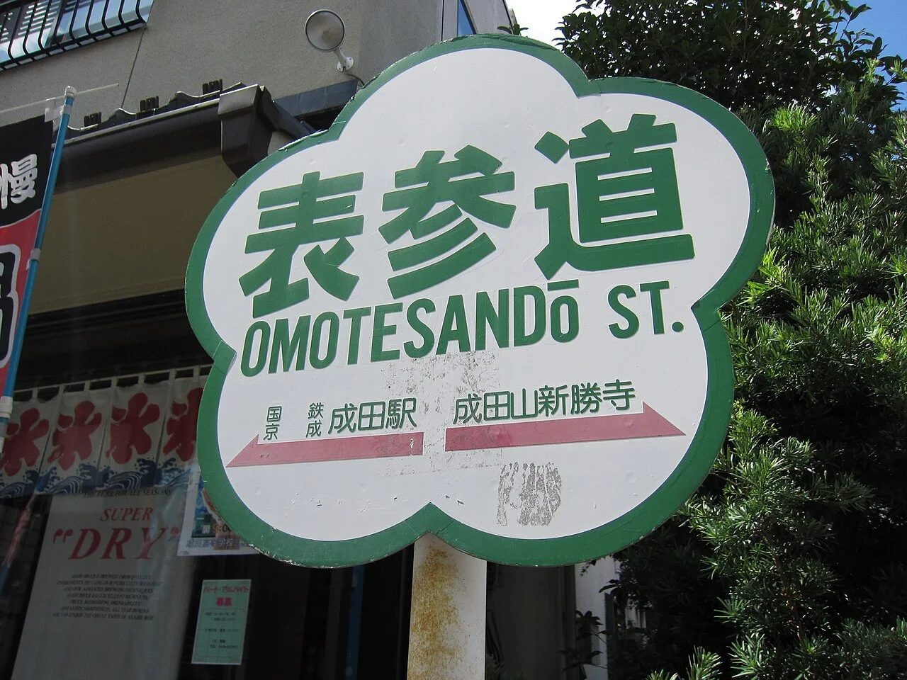 成田山表參道白底綠框花形街牌，附通往成田站與新勝寺的箭頭。