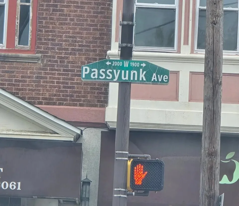 費城綠底白字Passyunk Ave街牌,上行可見2000、W、1900及雙向箭頭,下方為行人號誌。