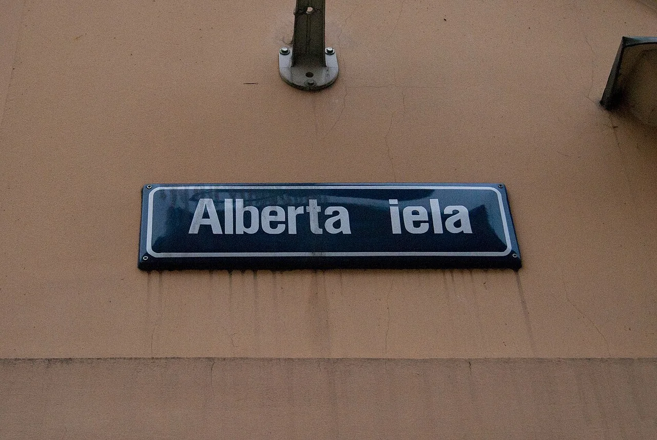 里加赭黃牆上的深藍Alberta iela路牌，白色粗字與圓角白色邊框。