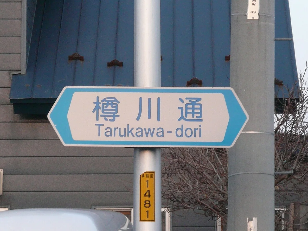 札幌手稻區樽川通的白底藍字街名牌,漢字下方列 Tarukawa-dori。