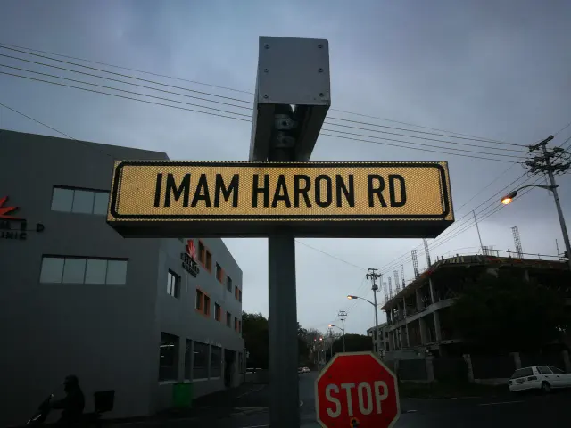 開普敦淡金色底黑字Imam Haron Rd街牌，下方為紅色STOP交通牌。