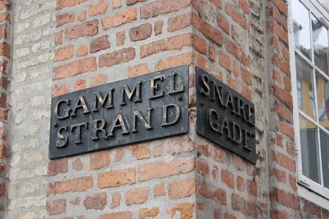 哥本哈根磚牆轉角兩面深色凸字街牌，分別寫Gammel Strand與Snaregade。