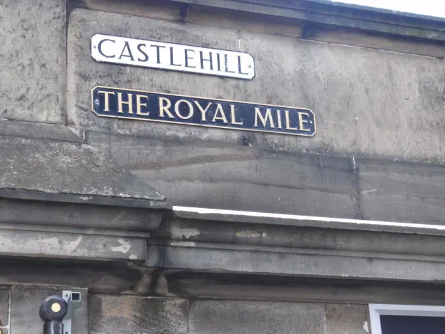 愛丁堡石牆上並列兩塊長牌，上方Castlehill白底黑字，下方The Royal Mile深底金字。
