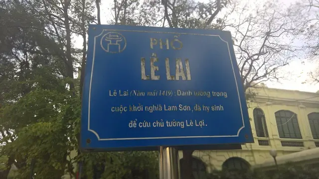 河內的藍白黎來街牌，上方寫 PHỐ LÊ LAI，同一牌面下方介紹黎來的生平。