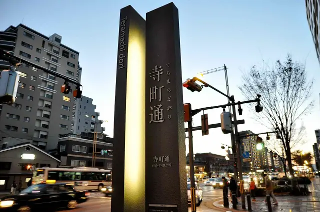 京都寺町通夜色中的黑色直立標示，寺町通直排文字與多語標示映在照明面板旁。