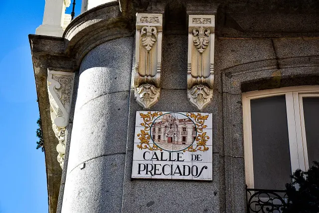馬德里Calle de Preciados彩繪磁磚街牌，上半部為建築圖與金色花飾，下半部為黑色街名。