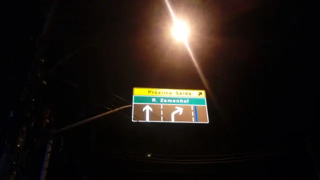 里約夜色中的綠色R. Zamenhof指路牌，上方黃色區寫Próxima Saída，下方有白色直行及右轉箭頭。