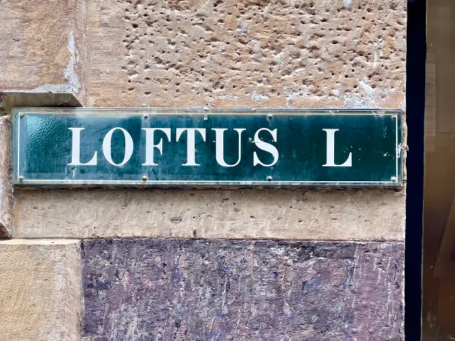 雪梨牆面上藍綠底白色襯線字Loftus L街牌，牌面帶反光，四周有框邊。