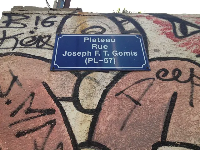 達卡塗鴉牆上的藍底白字街牌，依序寫Plateau、Rue、Joseph F. T. Gomis及PL–57。