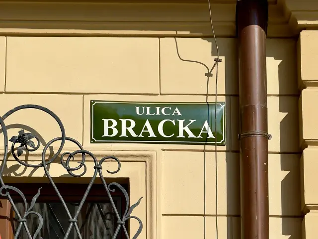 克拉科夫黃牆上的深綠街牌，上寫ULICA，下方大字BRACKA，四角有內縮白框。