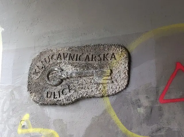 盧比安納鎖匠街的粗糙淺色牌，中央是一把立體鑰匙，上下有KLJUČAVNIČARSKA ULICA字樣。