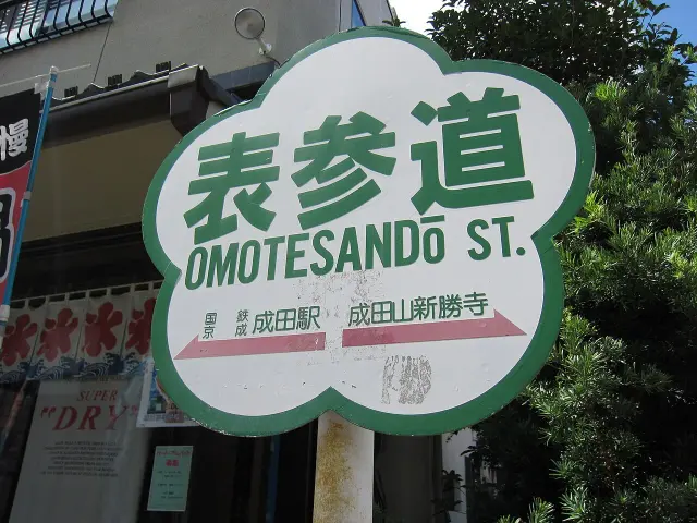 成田山表參道白底綠框花形街牌，附通往成田站與新勝寺的箭頭。