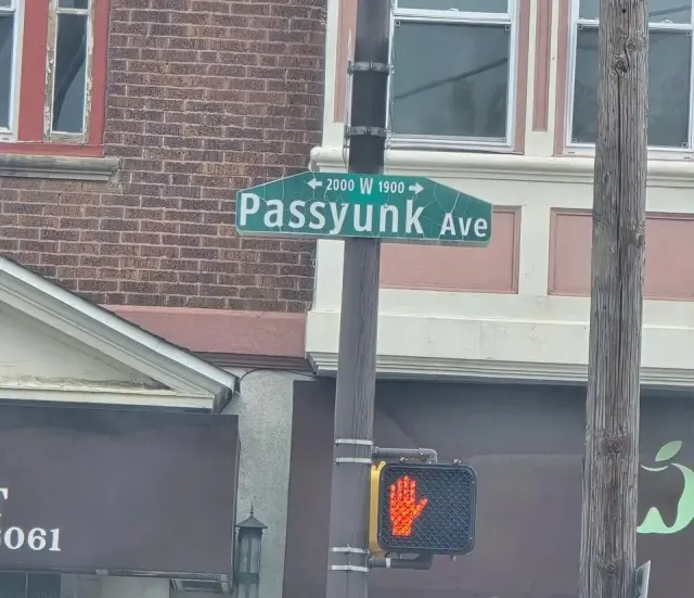 費城綠底白字Passyunk Ave街牌，上行可見2000、W、1900及雙向箭頭，下方為行人號誌。