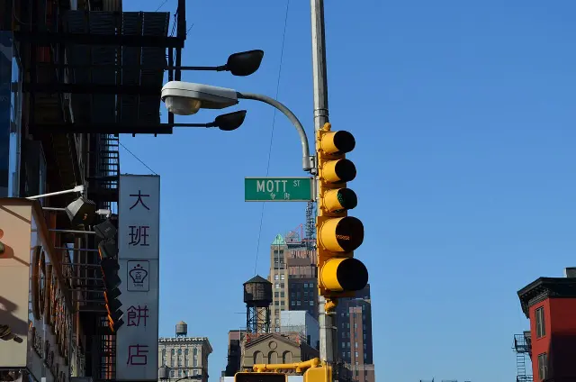 紐約華埠街角的綠色MOTT ST街名牌，下方有中文勿街，右側是黃色交通號誌。