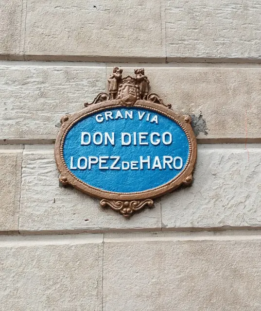 畢爾包石牆上的藍底橢圓街牌，分行寫GRAN VIA DON DIEGO LOPEZ DE HARO，頂端帶徽飾。