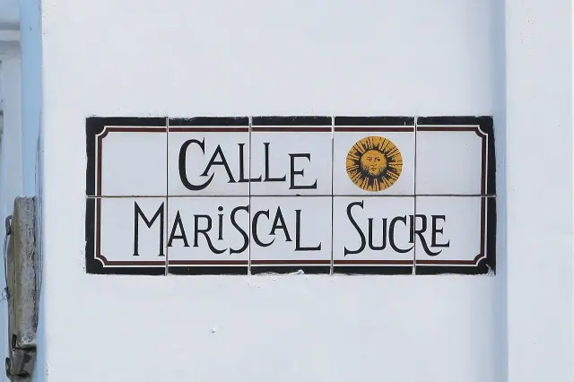 昆卡白色方磚拼成的CALLE MARISCAL SUCRE街牌，黑色裝飾字旁有金色太陽。