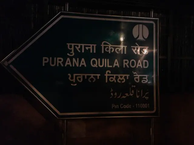 夜間拍攝的德里老堡路綠色箭頭牌，四行文字包含PURANA QUILA ROAD，底部標郵遞區號110001。