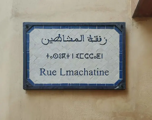 非斯的實拍街牌。下行「Rue Lmachatine」為街名；上方是阿拉伯文，中行以提非納文字母書寫阿馬齊格語。照片沒有門牌數字。