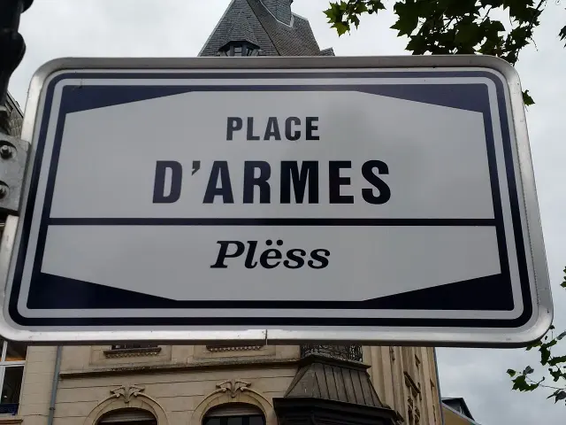 盧森堡市的實拍街牌。「PLACE D’ARMES」是法文武器廣場；下方斜體「Plëss」是盧森堡語通行名稱。