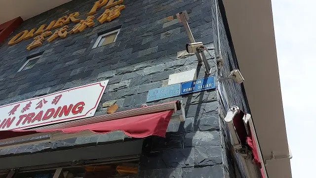 路易港石牆上的藍色RUE REMY OLLIER街牌，旁邊保留EX 12 RUE DES LIMITES舊牌，上方有淡色漢字。