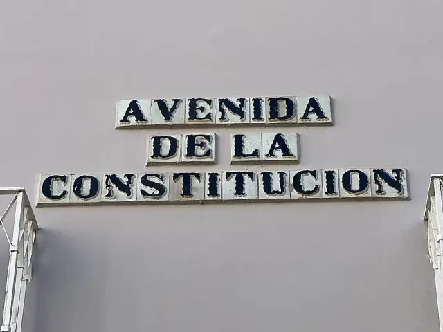 塞維亞灰牆上的乳白瓷磚街牌，以深色裝飾字寫AVENIDA DE LA CONSTITUCION。