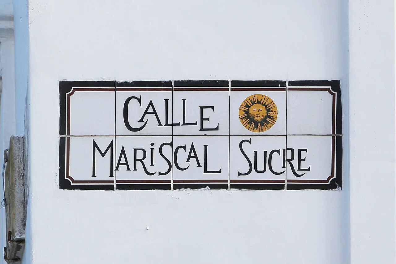 昆卡白色方磚拼成的CALLE MARISCAL SUCRE街牌，黑色裝飾字旁有金色太陽。