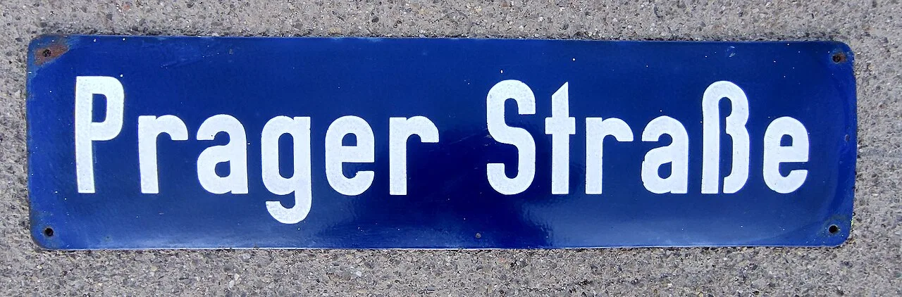 德勒斯登布拉格街的藍底白字舊牌平放在粗糙地面上，文字為Prager Straße。