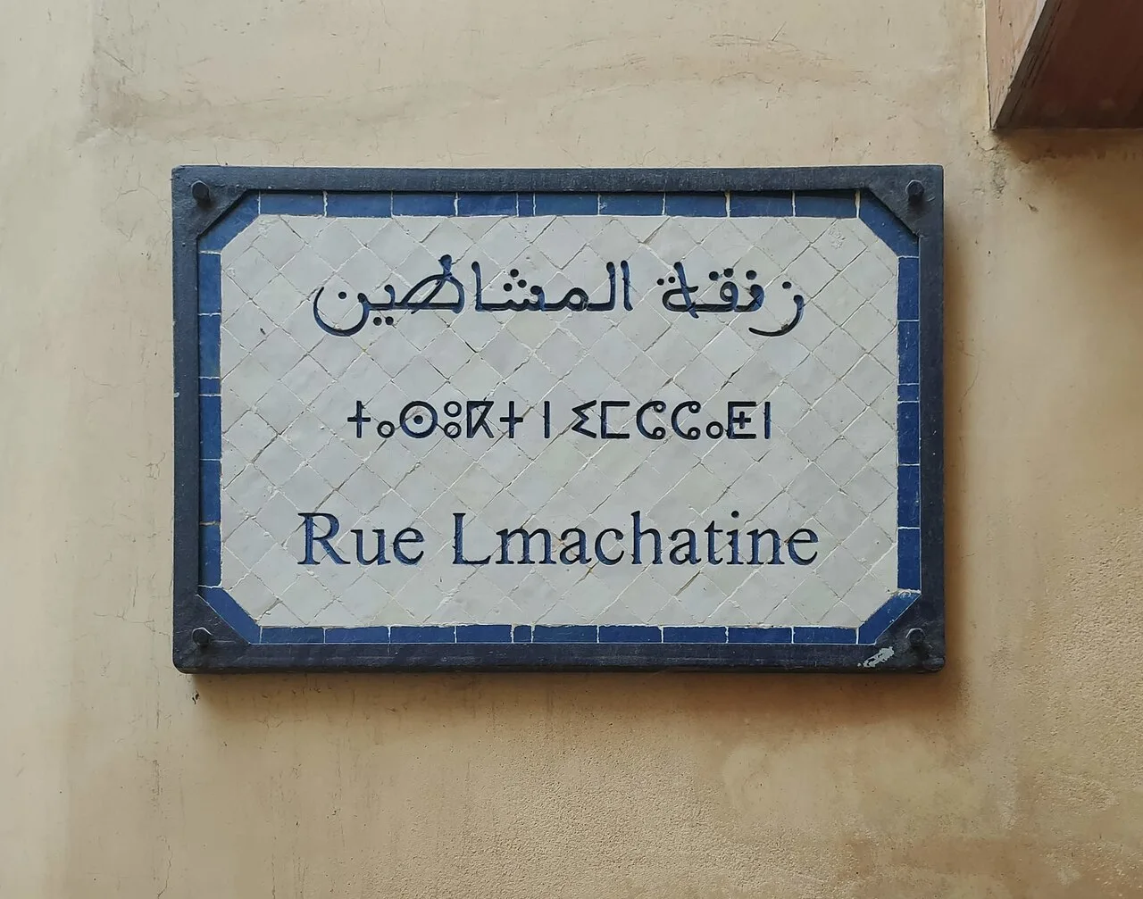 非斯的實拍街牌。下行「Rue Lmachatine」為街名;上方是阿拉伯文,中行以提非納文字母書寫阿馬齊格語。照片沒有門牌數字。