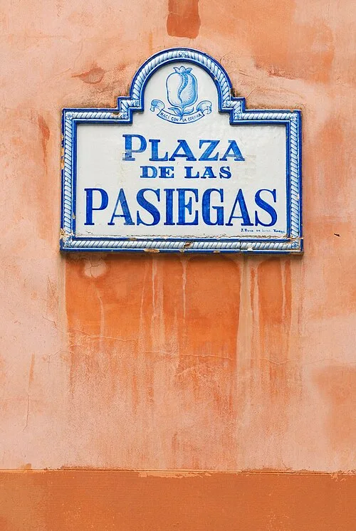 格拉納達橘牆上的藍白瓷磚街牌,寫有PLAZA DE LAS PASIEGAS並飾石榴圖案。