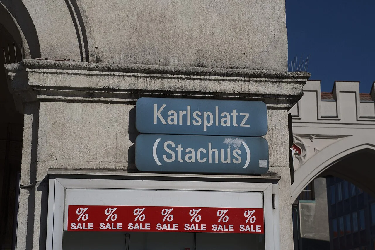 慕尼黑的實拍街牌。上牌「Karlsplatz」為卡爾廣場,下牌「(Stachus)」保留通行俗稱;括號不是另一個地址。