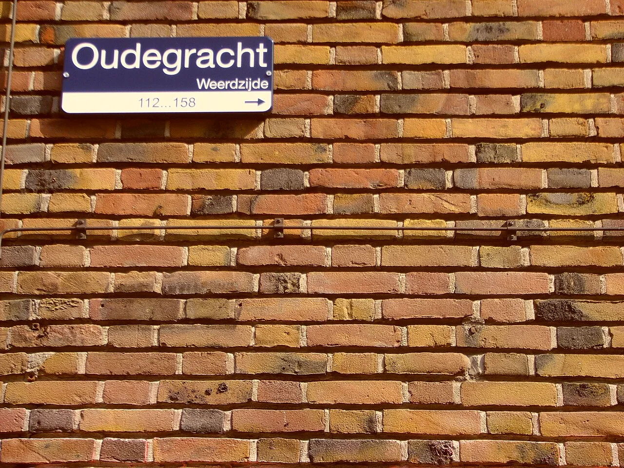 烏特勒支紅磚牆上的藍白街牌,寫有Oudegracht、Weerdzijde,下方112…158與向右箭頭。